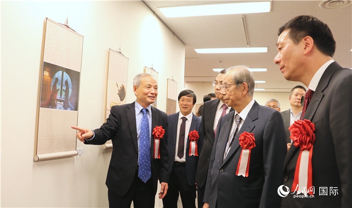 “湖州印象”攝影展主創(chuàng)、世界華人攝影協(xié)會副會長馮學(xué)敏向吳江浩大使、福田康夫前首相等嘉賓介紹展出作品。（人民網(wǎng) 許可攝）