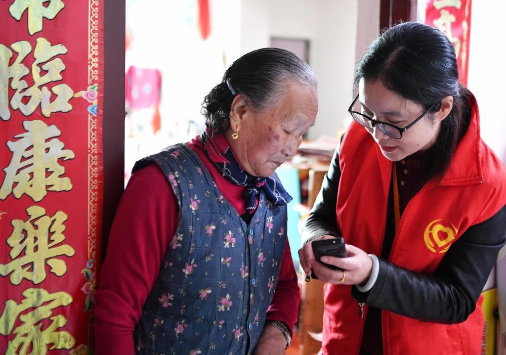 在福州市長樂區(qū)航城街道籌岐村，智慧養(yǎng)老平臺(tái)派駐社區(qū)的助老員（右）在為老人陳鳳英（左）講解養(yǎng)老定制手機(jī)的用法（2021年11月26日攝）。新華社記者 魏培全 攝
