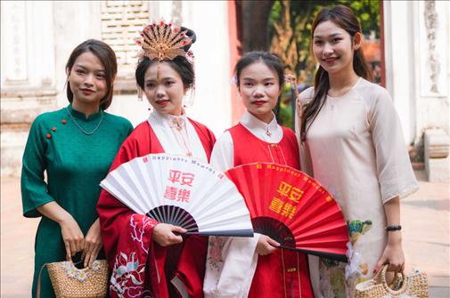 身穿古裝的中國游客和身穿越南傳統(tǒng)服飾奧黛的越南青年在文廟門前合影。
