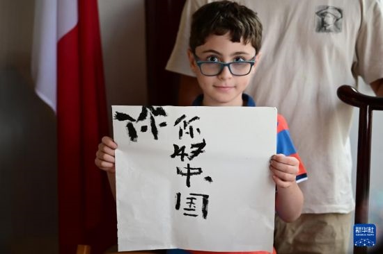 7月4日，在馬耳他桑塔露琪亞市的中國(guó)古典園林“靜園”，一名男孩展示他的書(shū)法作品。新華社發(fā)（喬納森·博格 攝）