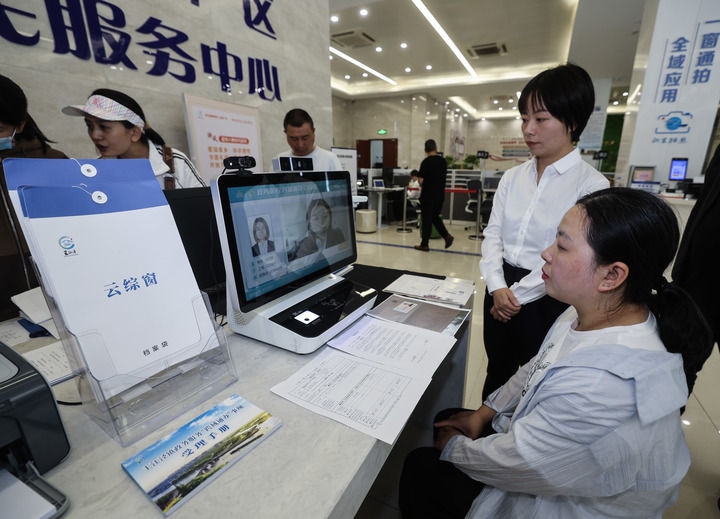 在浙江省嘉興市秀洲區(qū)王江涇鎮(zhèn)便民服務(wù)中心的“跨域通辦·云綜窗”窗口，辦理開業(yè)登記的個(gè)體工商戶（右一）通過該系統(tǒng)與江蘇省蘇州市吳江區(qū)盛澤鎮(zhèn)行政審批局工作人員視頻連線，進(jìn)行身份讀取及材料線上審核（2024年5月9日攝）。新華社記者 徐昱 攝