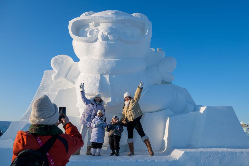 2025年1月3日，在黑龍江哈爾濱冰雪大世界園區(qū)，游客與亞冬會吉祥物雪雕“濱濱”合影