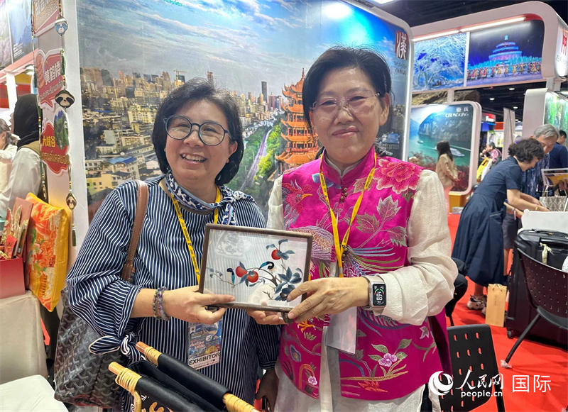 中國“大冶刺繡”傳承人劉小紅（右）參加泰國國際旅游展，向觀眾介紹中國非遺刺繡針法。人民網記者 簡承淵攝